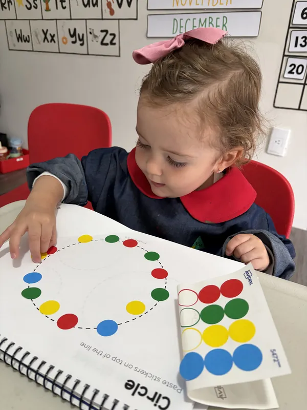 Niña pegando estampas de colores en su libro de trabajo