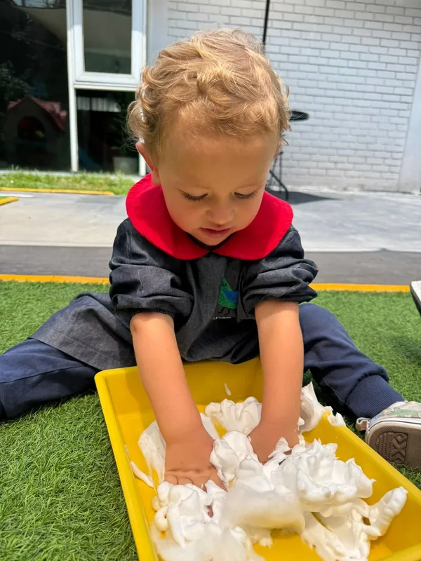 Niño jugando con espuma en una charola amarilla