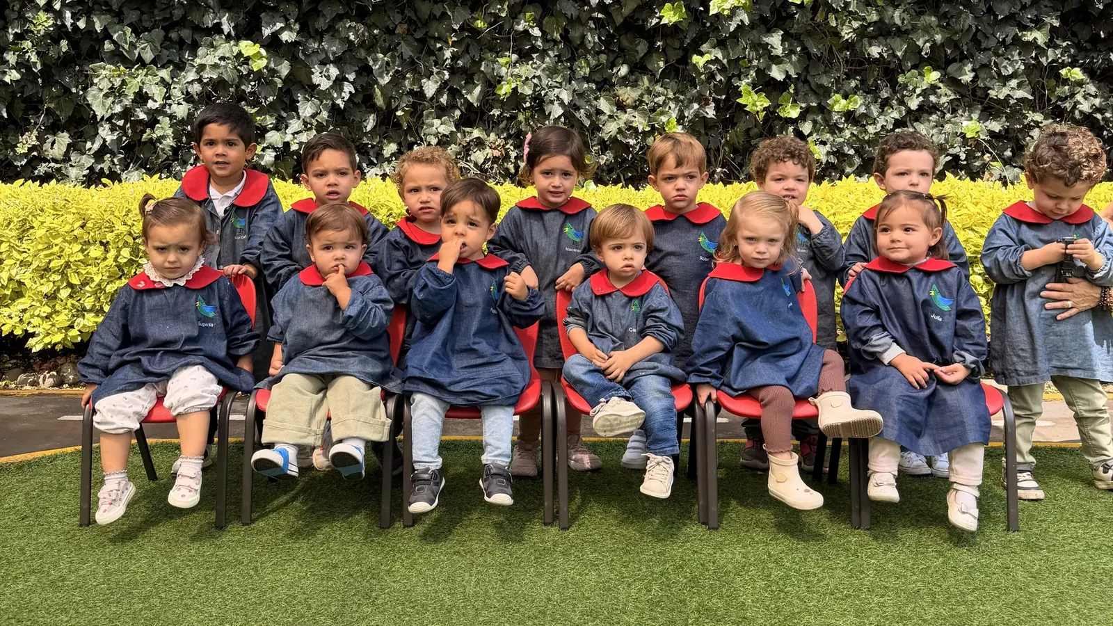 Grupo de niños de Piruli con su uniforme, sentados en sillitas rojas en el jardín